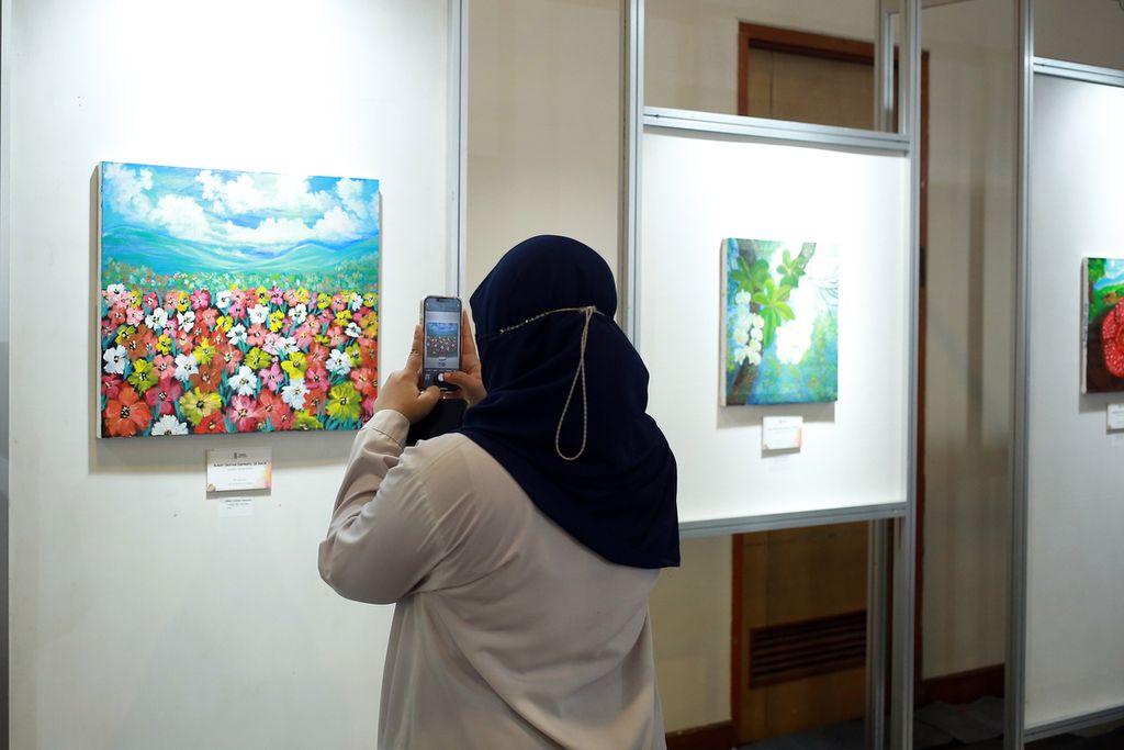 Pengunjung memotret lukisan yang dipajang dalam acara Karya Tanpa Batas di Smesco Indonesia, Jakarta Selatan, Selasa (20/12/2022). 