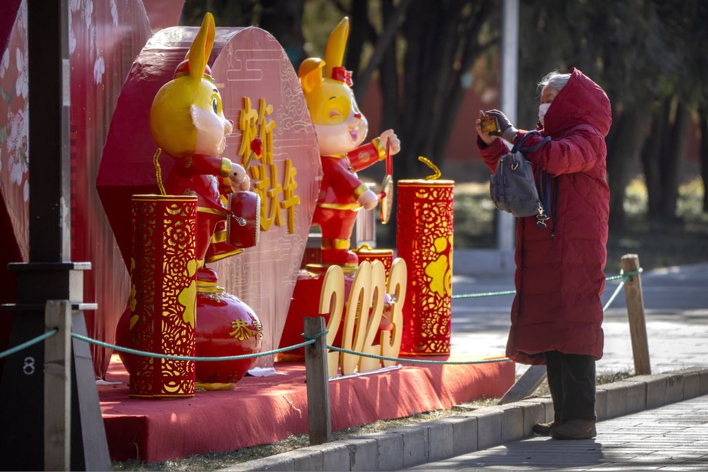 Seorang perempuan mengambil foto dengan ponselnya untuk Tahun Baru Imlek di sebuah taman umum di Beijing, China, Jumat (20/1/2023). 