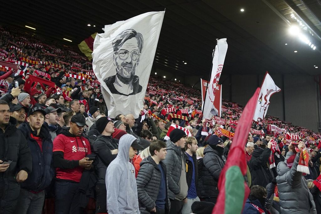 Suporter Liverpool mengibarkan bendera bergambar Manajer Liverpool Jurgen Klopp dalam pertandingan laga pertama semifinal Piala Liga Inggris melawan Arsenal di Stadion Anfield, Liverpool, Kamis (13/1/2022).