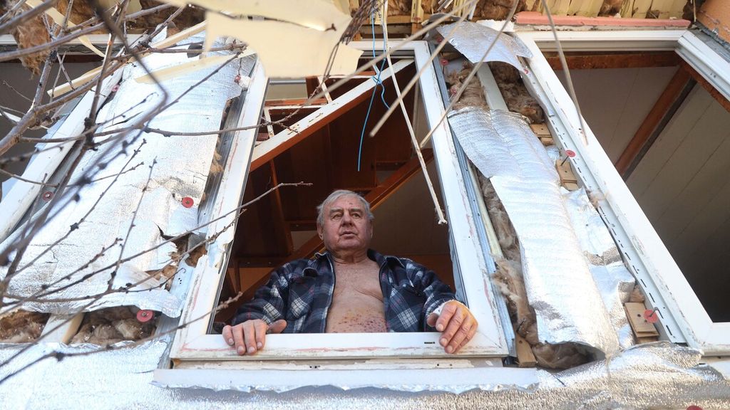 Seorang pria melihat keluar dari jendela rumahnya yang sebagian telah hancur setelah penembakan oleh kapal perang Rusia, di pinggiran Odessa, Senin (21/3/2022). Kecuali Lviv dan Odessa, nyaris semua kota utama Ukraina sudah dikepung pasukan Rusia.