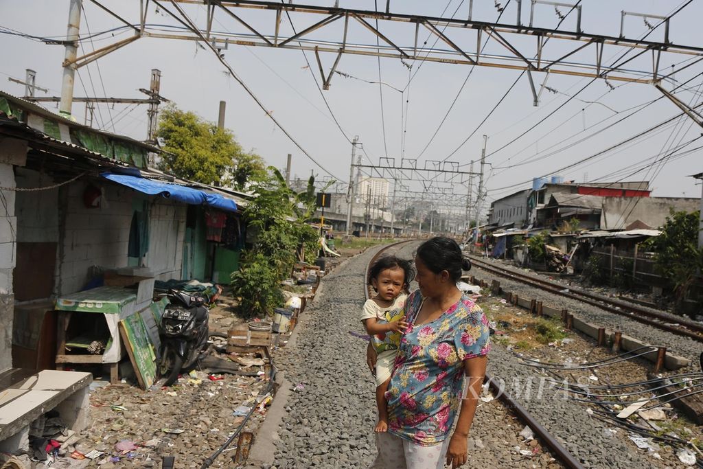 Ibu dan anak di ruang terbuka di antara jalur kereta yang membelah hunian semipermanen padat penduduk di kawasan Pademangan, Jakarta Utara, Kamis (17/7/2023). 