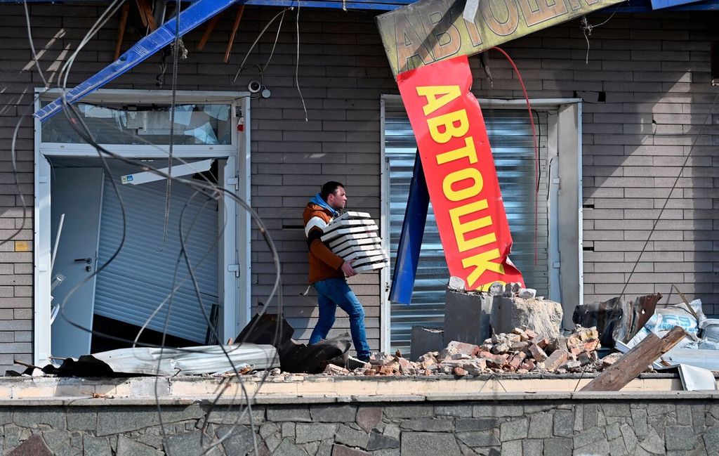 Seorang pria membawa kotak pizza kosong dari sebuah kafe setelah serangan Rusia menghancurkan sejumlah pertokoan di Kiev, Ukraina, Kamis (17/3/2022).