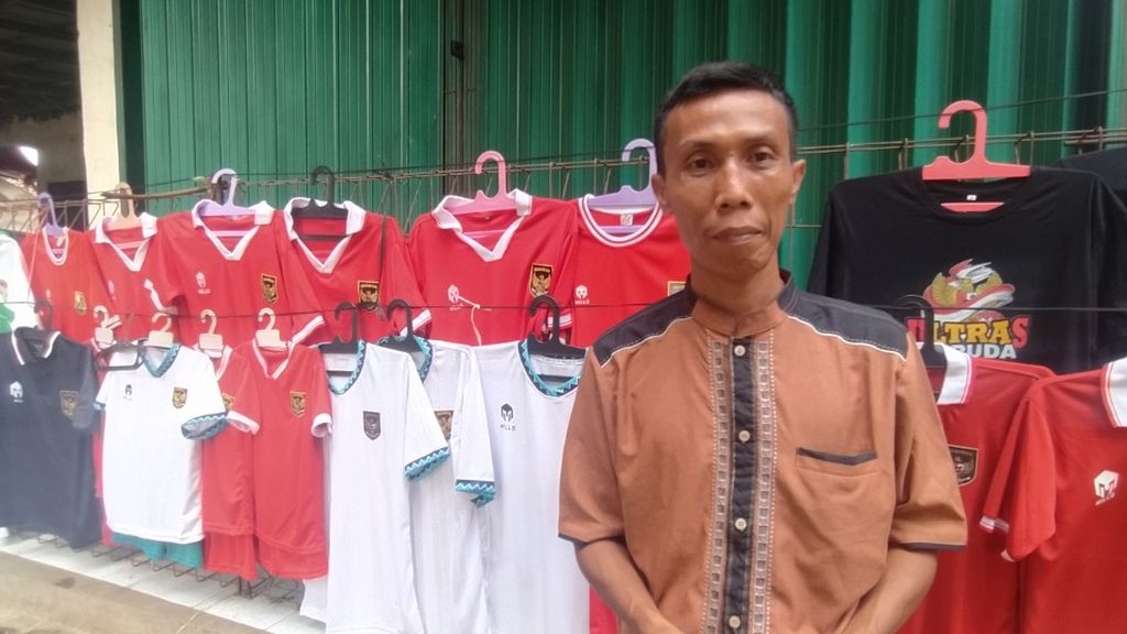 Hakim (40) tengah berjualan kaos sepak bola di sekitar Stadion Pakansari, Kabupaten Bogor, Jawa Barat, Minggu (9/10/2022). Ia rela pulang-pergi setiap harinya ke Tasikmalaya, Jawa Barat demi mendapatkan penghasilan dari berjualan kaos.