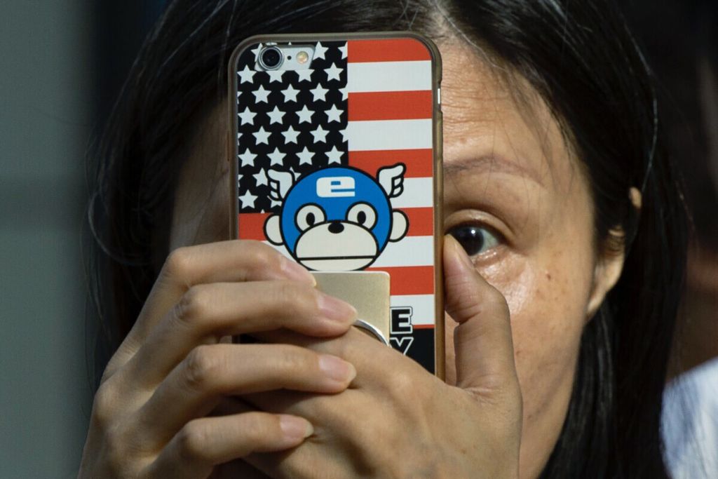 Seorang wanita mengambil foto dengan ponsel yang memiliki sampul bertema bendera Amerika Serikat di luar Konsulat Amerika Serikat di Chengdu,  Sichuan pada Minggu (26/7/2020). Selain perang dagang, relasi AS dan China diwarnai ketegangan termasuk terkait isu Laut China Selatan, Uighur, Hong Kong, dan mata-mata.