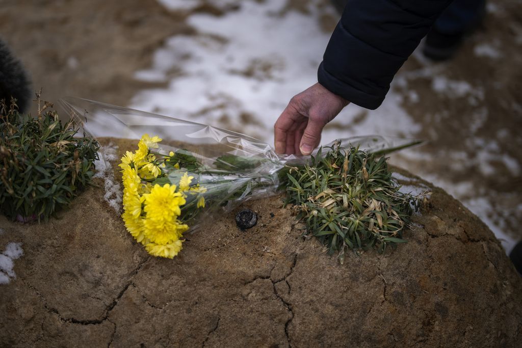 Seorang laki-laki tengah meletakkan karangan bunga di atas makam kerabatnya di Bucha, Ukraina, Jumat (24/2/2023). 