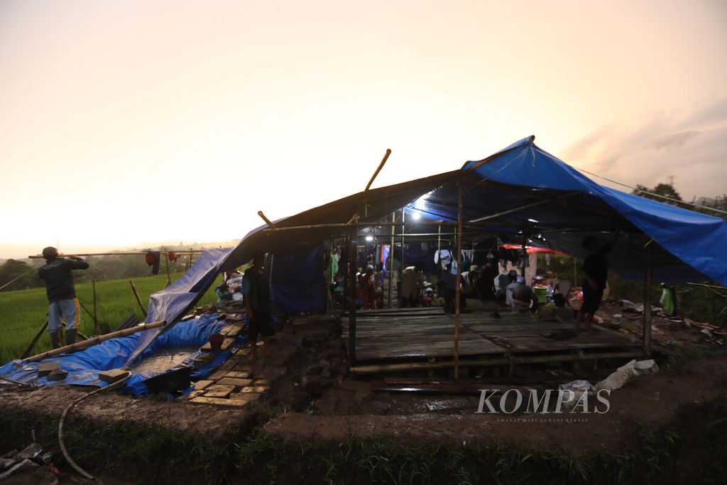 Warga memperbaiki tenda pengungsian yang rusak karena angin kencang di lahan perkebunan dan persawahan di Desa Cibeureum, Kecamatan Cugenang, Kabupaten Cianjur, Senin (28/11/2022). 