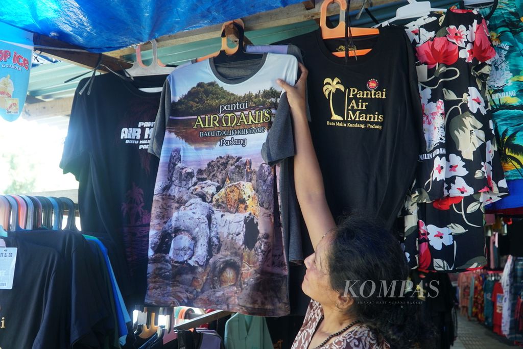 Pedagang tengah menggantungkan kaus bergambar obyek wisata batu Malin Kundang di lapaknya, Pantai Air Manis, Kota Padang, Sumatera Barat, Senin (28/8/2023). 