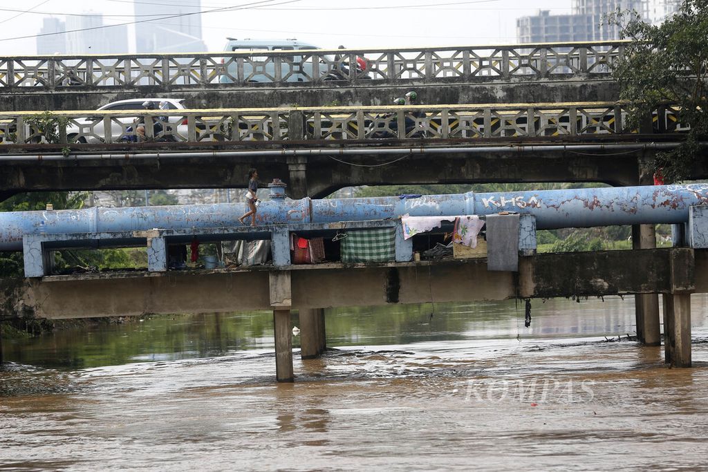 Warga miskin beraktivitas pada jembatan pipa air bersih yang merangkap sebagai tempat tinggalnya di atas Sungai Ciliwung di kawasan Tanah Abang, Jakarta, Minggu (16/10/2022).