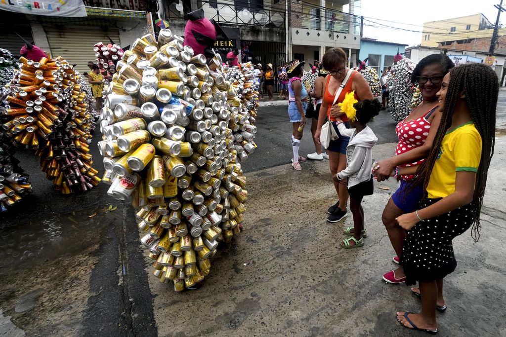 Warga memperhatikan para pengguna <i>pierro</i>, kostum yang dibuat dari serangkaian kaleng bekas minuman, pada karnaval jalanan yang diselenggarakan di Kota Madre de Deus, Brasil, Minggu (11/2/2024). 