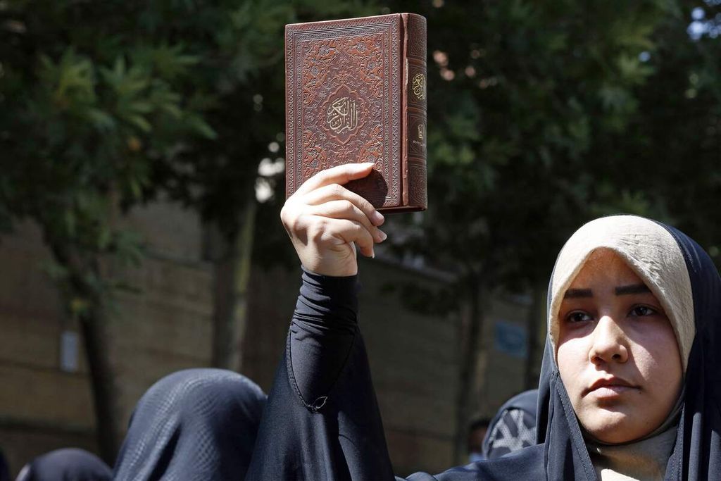 Seorang warga Iran membawa Al Quran dalam unjuk rasa di luar Kedutaan Besar Swedia untuk Iran di Teheran, Iran, 30 Juni 2023, guna memprotes pembakaran Al Quran di Swedia. 