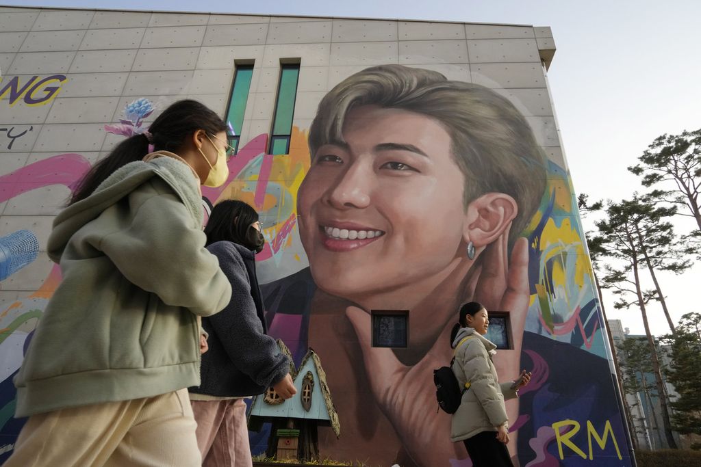 Orang-orang berjalan melewati mural bergambar RM, anggota band <i>K-pop</i> BTS di Goyang, Korea Selatan, pada 10 Desember 2023.