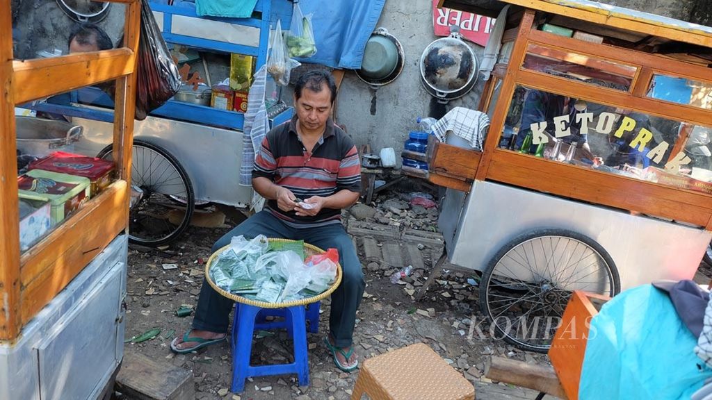 Toyo (50) membuat lontong pada Senin (10/6/2019) di antara gerobak dorong yang menjajakan aneka jajanan di Jalan Swasembada Timur IV, Kecamatan Kebon Bawang, Tanjung Priok, Jakarta Utara.