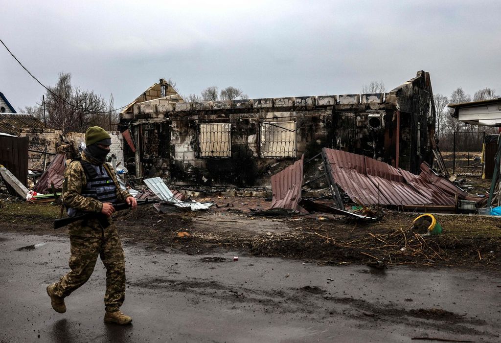 Seorang tentara Ukraina berpatroli di dekat rumah yang terbakar di Desa Lukianivka, dekat Kyiv, Rabu (30/3/2022). 
