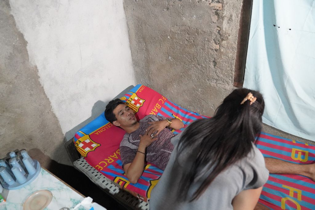 Muhammad Syafi’i (32) sedang diobati Dinda, istrinya, di rumahnya di Desa Selorejo, Kabupaten Gunungkidul, DI Yogyakarta, Rabu (26/7/2023). Syafi'i saat ini menderita kerusakan saraf pada bagian tubuhnya imbas dari kecelakaan kerja yang dia alami ketika menjadi anak buah kapal migran di kapal China pada pertengahan 2021. 