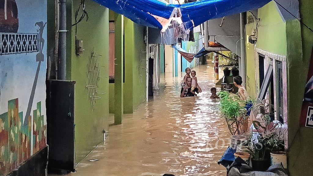 Seorang ayah mengendong dua anak keluar dari banjir di Kebon Pala, Kampung Melayu, Jatinegara, Jakarta Timur, Kamis (30/11/2023).
