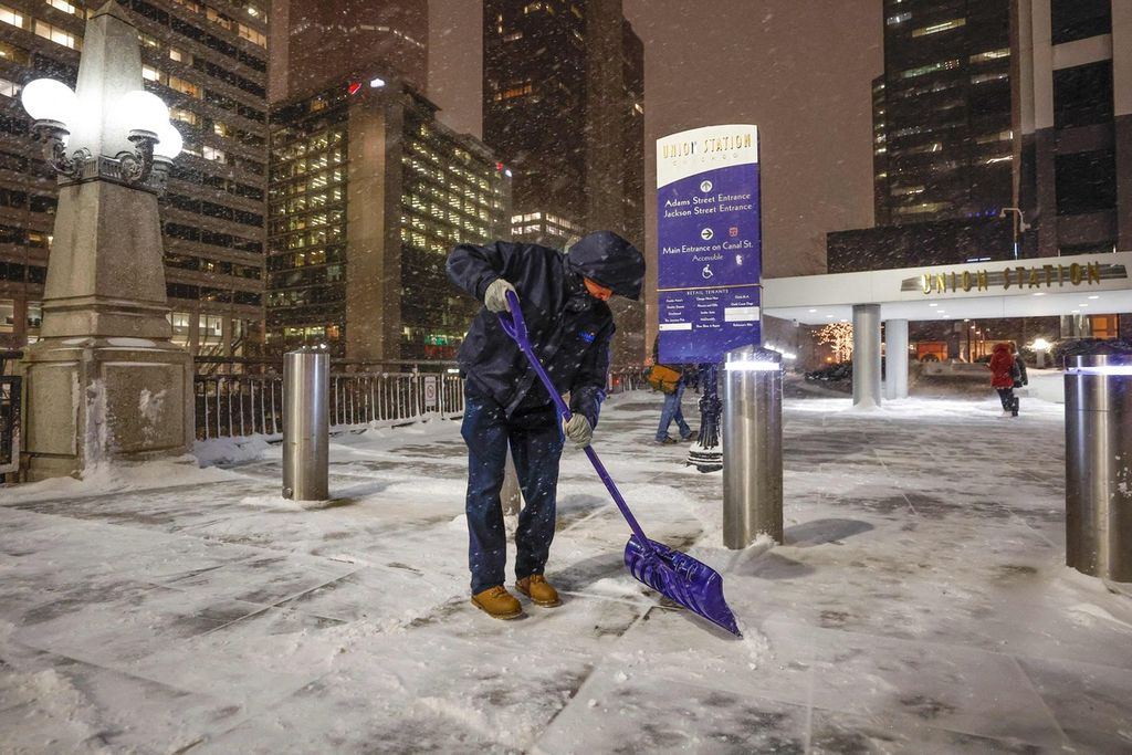 Seorang warga tengah membersihkan pedestrian di luar Stasiun Union, Chicago dari tumpukan salju, Kamis (22/12/2022).