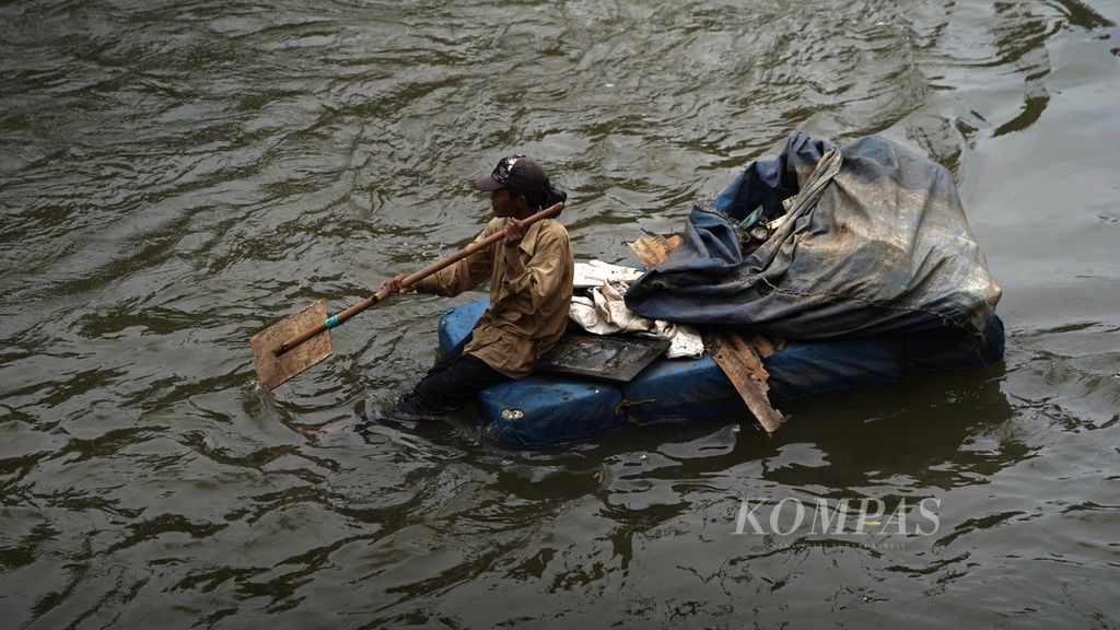 A scavenger man uses a canoe made of streofom material to search for used goods that have washed away in the Ciliwung River in Tebet, South Jakarta, Tuesday (7/2/2023).
