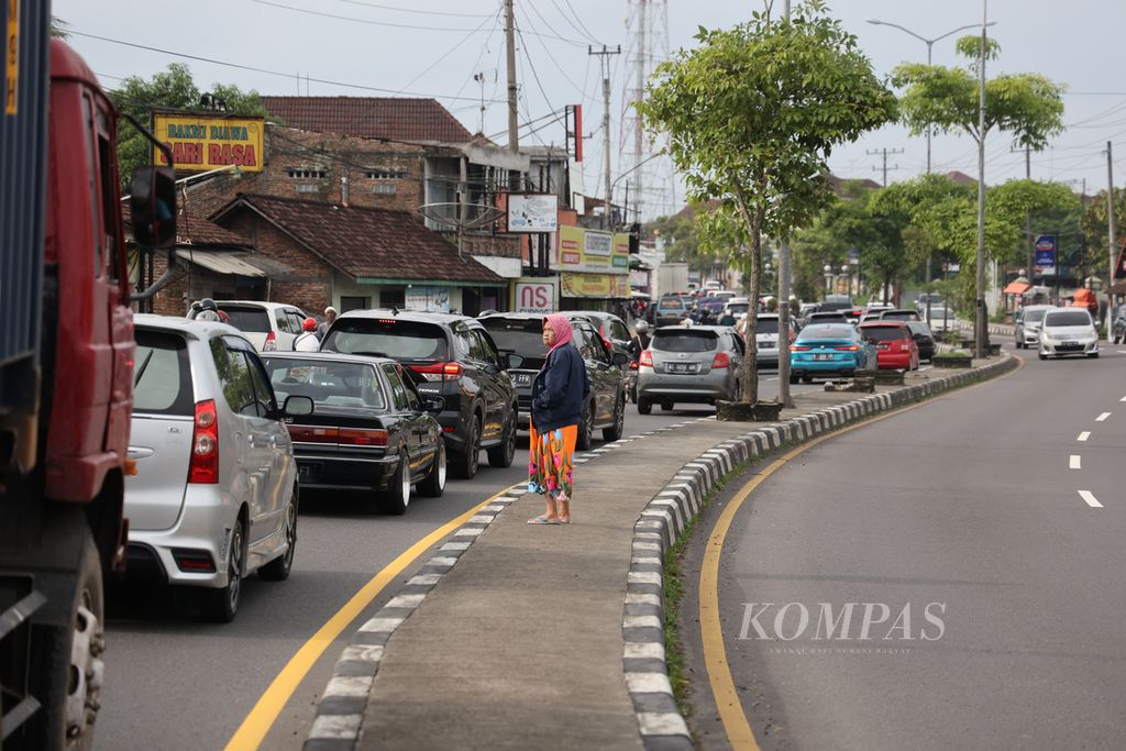 Seorang warga lansia menunggu kesempatan menyeberang saat kendaraan berjalan merayap di Jalan Raya Blabak-Magelang, Kecamatan Mungkid, Kabupaten Magelang, Jawa Tengah, Minggu (1/1/2023) sore.  