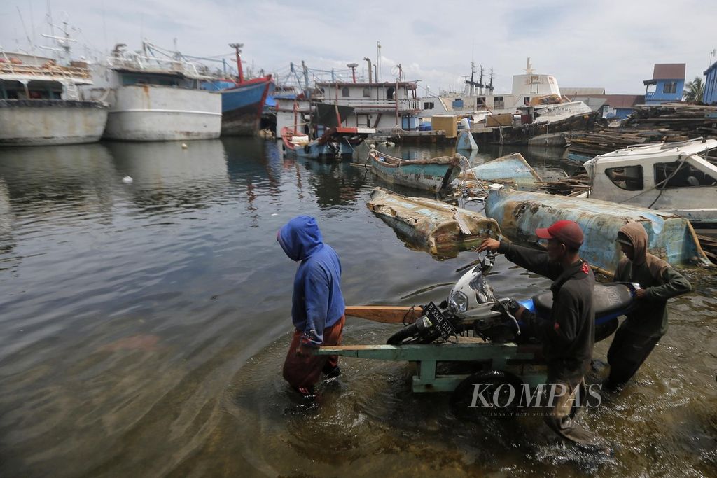 Tukang gerobak menawarkan jasa mengangkut sepeda motor saat banjir rob menggenangi beberapa tempat di kawasan Pelabuhan Perikanan Samudera Nizam Zachman, Jakarta Utara, Minggu (8/1/2023).