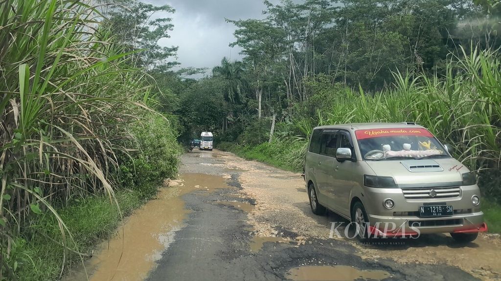 Mobil wisatawan melintas di jalanan rusak di Desa Srigonco, Kecamatan Bantur, Kabupaten Malang, Jawa Timur, Minggu (9/7/2023), yang berkubang setelah turun hujan.