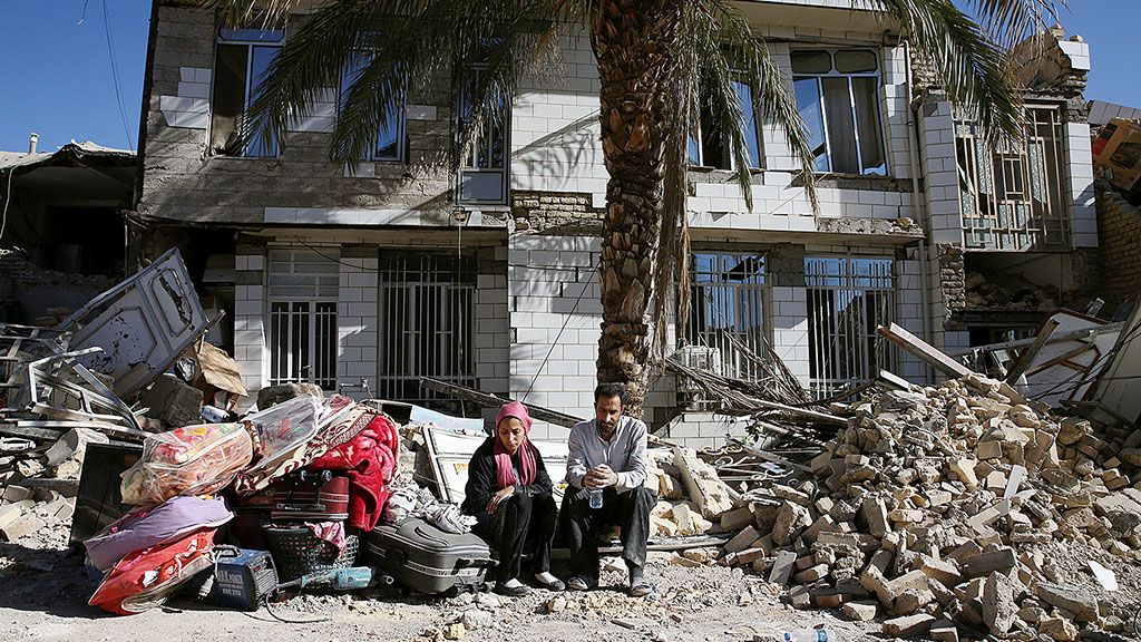 Dua warga  korban gempa duduk di depan rumah yang rusak di lokasi gempa di Sarpol-e-Zahab, Iran bagian barat, Selasa (14/11). Para anggota  penyelamat berupaya mencari korban dengan menggali puing-puing reruntuhan  gedung yang ambruk akibat guncangan gempa pada hari Minggu lalu di wilayah perbatasan Iran dan Irak.