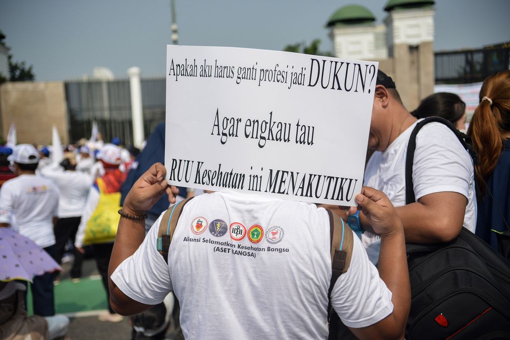 Seorang tenaga kesehatan (Nakes) membawa poster berisi pesan aksi di depan gedung DPR, Jakarta Pusat, Senin (5/6/2023).  
