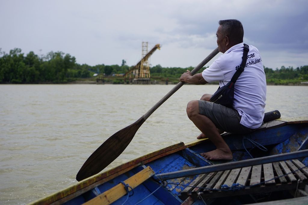 Mahmud (60), seorang nelayan, mendayung perahunya melewati pelabuhan batubara di perairan Teluk Balikpapan, Kaltim, Minggu (6/3/2022).
