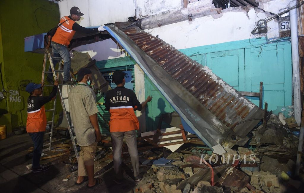 Petugas berusaha mencopot bagian atap bangunan yang rusak di Jalan Ngaglik  pascagempa di Surabaya, Jawa Timur, Jumat (22/3/2024). Gempa yang terjadi beberapa kali tersebut berpusat di laut dengan jarak 130 kilometer timur laut Tuban. Pada pukul 15.52, terjdi gempa berkekuatan magnitudo 6,5 dengan kedalaman 10 kilometer. Di Surabaya, sejumlah bangunan rusak.