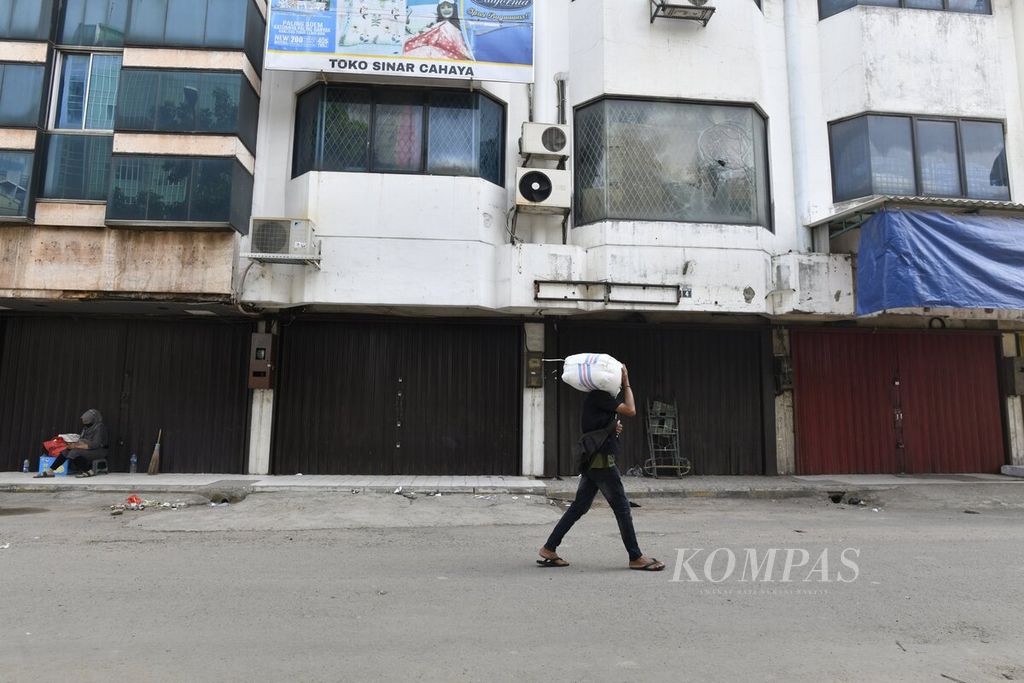 Pekerja membawa barang melewati deretan pertokoan dan perkantoran di kawasan Tanah Abang, Jakarta Pusat, yang tutup sementara, Kamis (8/7/2021). Sebagian besar pusat perekonomian tutup sementara selama masa PPKM darurat Jawa-Bali pada 3-20 Juli. 