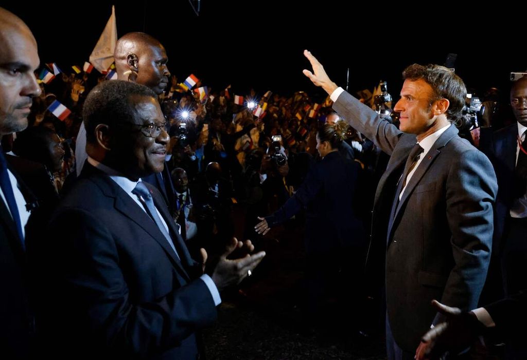 Presiden Perancis Emmanuel Macron (kanan) melambaikan tangan ke arah kumpulan warga saat disambut Perdana Menteri Kamerun Joseph Dion Ngute (kedua dari kiri) di Bandar Udara Internasional Nsimalen, Yaounde, Kamerun, Senin (25/7/2022). 