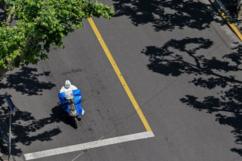 Seorang pekerja dengan mengenakan alat pelindung diri lengkap mengendarai sepeda motor di jalanan Shanghai, China, yang sepi pada tanggal 5 Mei 2022. Kota itu masih melakukan aturan penguncian wilayah guna mencegah penularan Covid-19. 