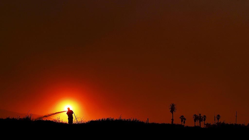 Petugas pemadam  kebakaran  dipotret secara siluet dengan latar belakang matahari saat ia berjuang memadamkan api di dekat Faria State Beach, Ventura, Negara Bagian California, Amerika Serikat, Kamis (7/12). Tiupan angin kencang pada api menyebabkan puluhan rumah rusak dan puluhan ribu warga dievakuasi.  