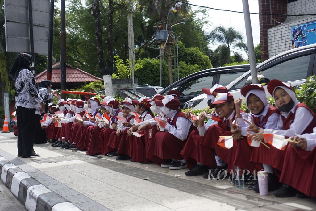 Anak-anak sekolah duduk berjejer memegang bendera Merah Putih saat menunggu Presiden Joko Widodo melintas di Pasar Klandasan, Kota Balikpapan, Kalimantan Timur, Selasa (25/10/2022).