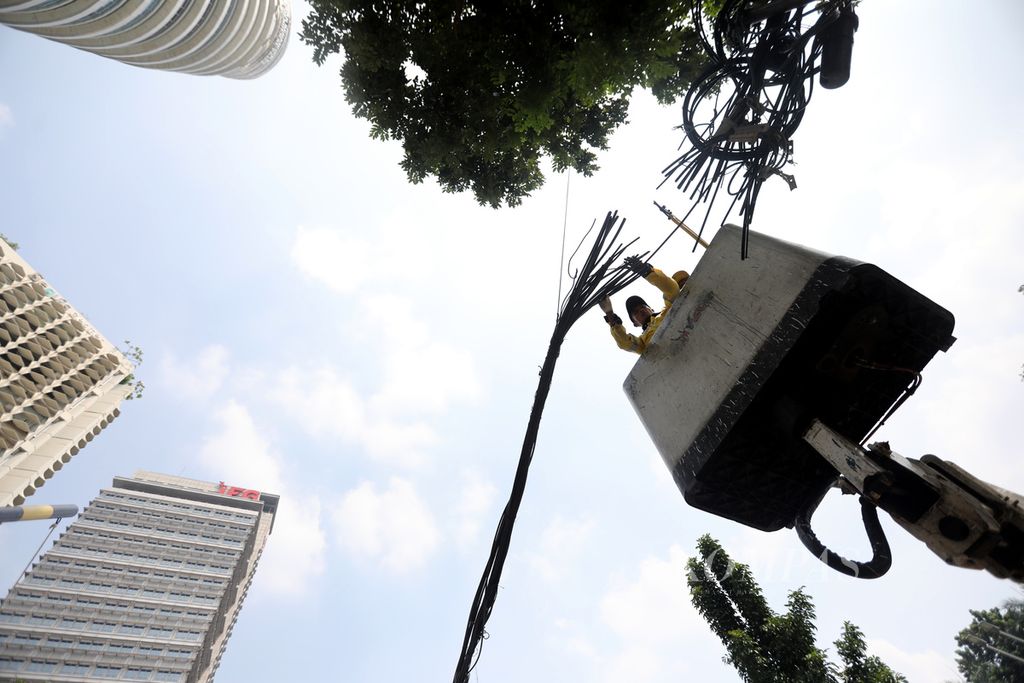 Petugas Dinas Bina Marga memotong kabel utilitas yang dibersihkan dari tiang-tiang di kawasan Jalan Jenderal Sudirman, Jakarta Selatan, Selasa (9/5/2023).  