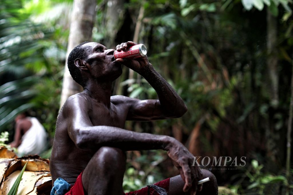 Abarham Jip menenggak minuman kaleng bersoda saat bersama warga kampung As dan Atat, Distrik Pulau Tiga, Asmat, Papua, memangkur sagu di hutan adat mereka, Kamis (14/10/2021).