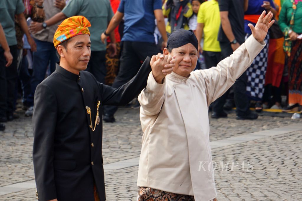 Presiden Joko Widodo dan Prabowo Subianto bergandengan dan melambaikan tangan.
