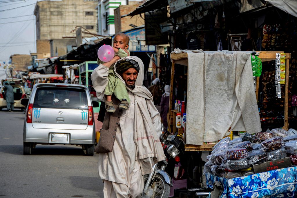 Seorang laki-laki, warga Afghanistan, menggendong anaknya yang tengah bermain balon di pundaknya saat tengah berjalan di Kandahar, Afghanistan, Sabtu (12/3). 