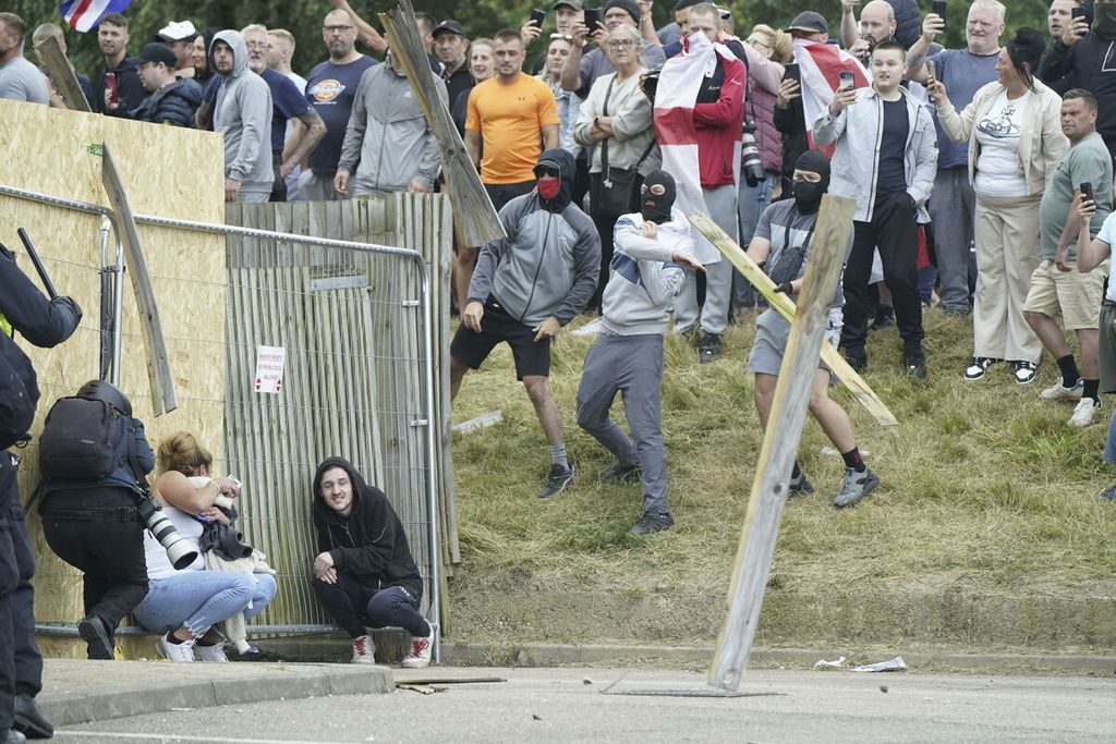 Seorang wanita dan seorang laki-laki berlindung saat pengunjuk rasa melemparkan benda-benda dalam aksi unjuk rasa anti-imigran di luar hotel Holiday Inn Express di Rotherham, Inggris, MInggu (4/8/2024).