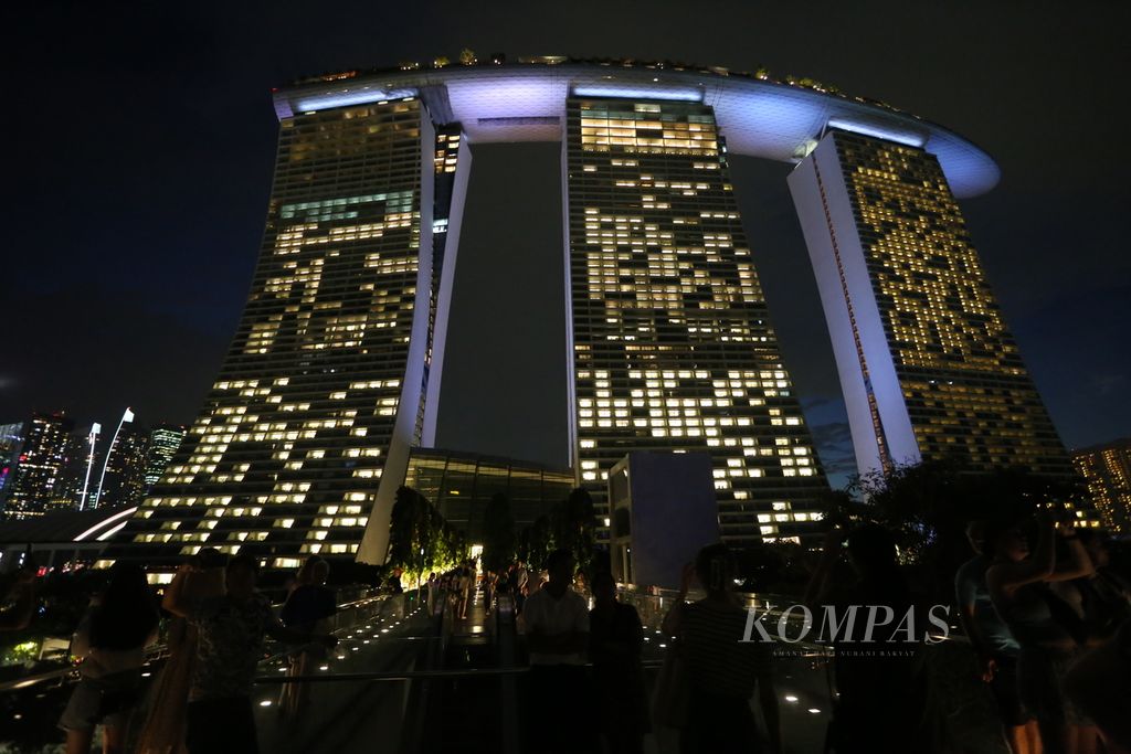 Wisatawan menikmati pemandangan malam di sekitar Hotel Marina Bay Sands di Bayfront Ave, Singapura, Rabu (5/7/2023). Kawasan yang dibangun di atas lahan reklamasi ini sekarang telah berkembang pesat dan menjadi tujuan wisata populer Singapura.