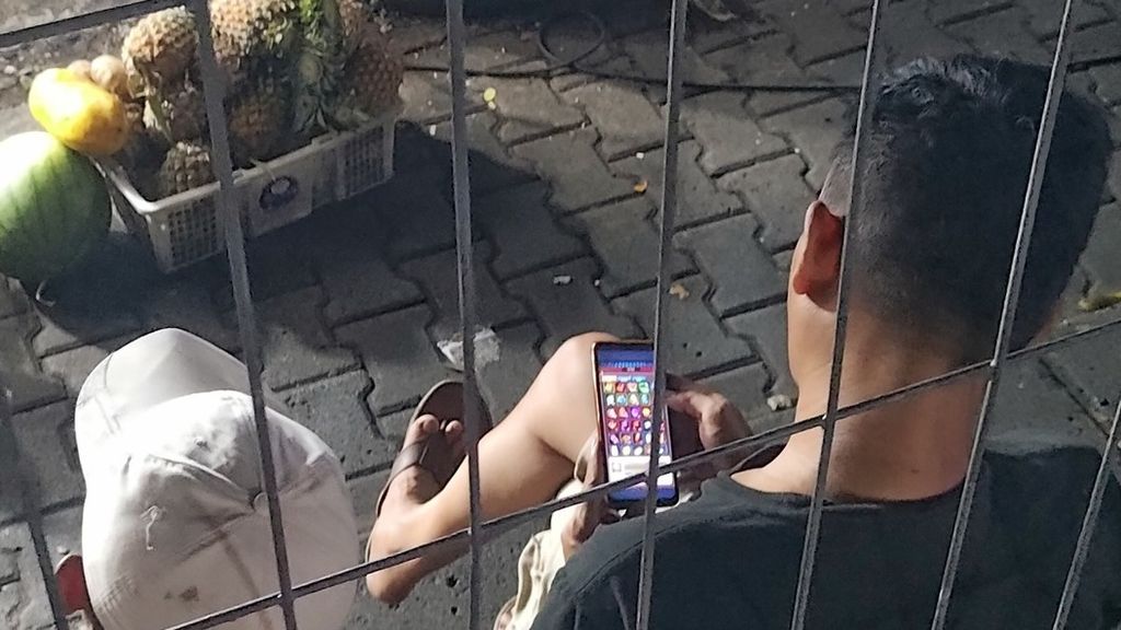 Seorang laki-laki tampak membuka situs judi slot lewat ponselnya ketika berada di daerah Jakarta Selatan, Jumat (24/11/2023). 