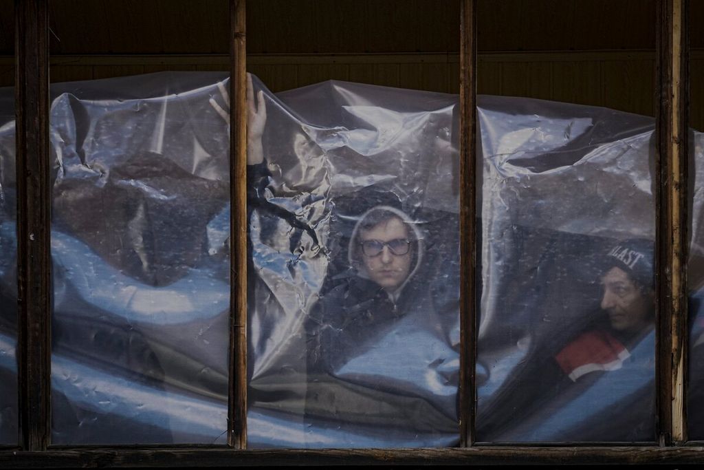 Penghuni apartemen memasang lembaran plastik untuk menutupi jendela yang pecah di apartemen mereka setelah bagian dari rudal Rusia yang ditembak jatuh oleh pertahanan udara Ukraina mendarat di sebuah blok apartemen di Kiev, Ukraina, Kamis (17/3/2022). 