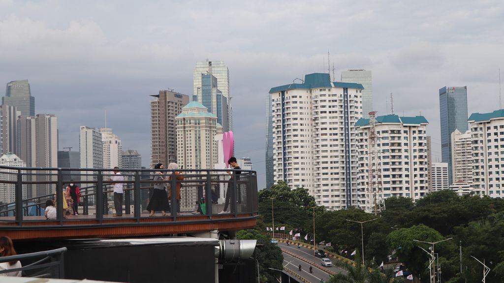 Warga menikmati pemandangan gedung tinggi di Jakarta dari jembatan Skywalk di atap gedung Mal Senayan Park, Jakarta Pusat, Rabu (8/2/2023).