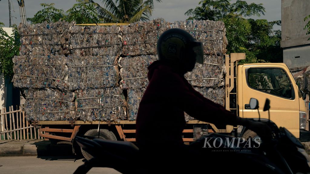 Warga melintasi sampah plastik minuman kemasan yang akan dibawa dengan truk di Tanah Tinggi, Kota Tangerang, Banten, Minggu (23/1/2022). 