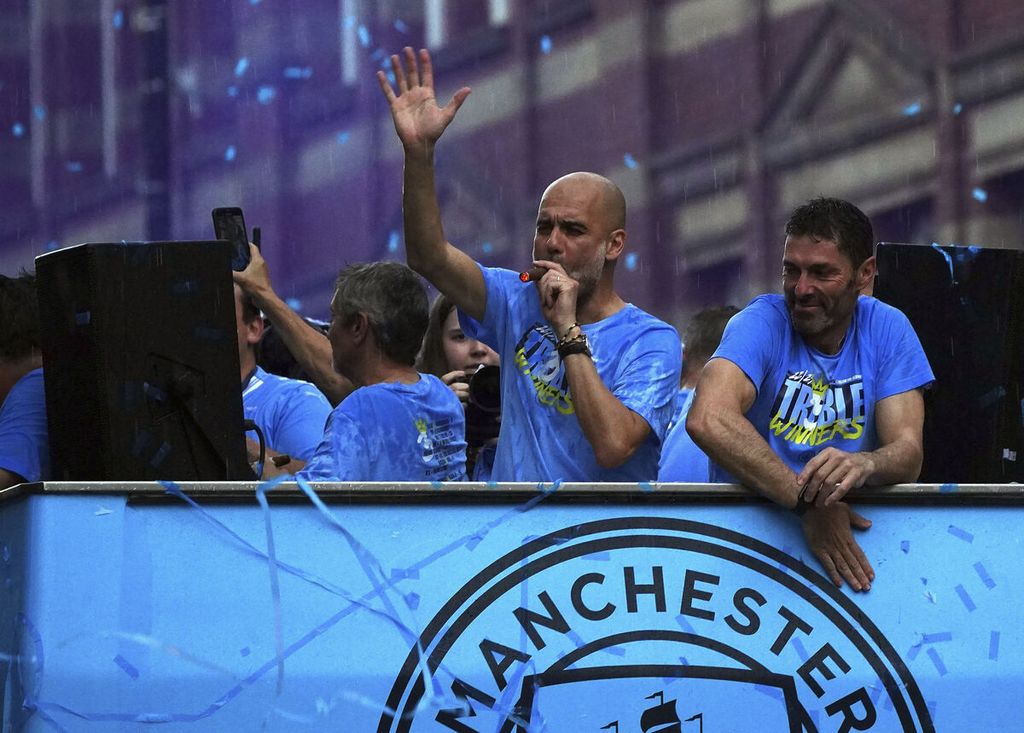 Manajer Manchester City Pep Guardiola mengisap cerutu di samping pelatih kiper Xabier Mancisidor selama pawai merayakan Liga Primer, Piala FA, dan Liga Champions di Manchester, England, Senin (12/6/2023). 