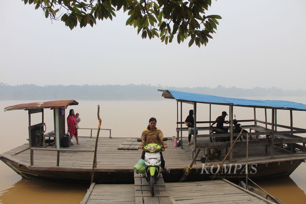 Warga Desa Simpur, Kabupaten Pulang Pisau, Kalimantan Tengah, menggunakan kapal feri kayu untuk menyeberangi Sungai Kahayan, bahkan di tengah kabut asap akibat karhutla, Selasa (3/10/2023). 