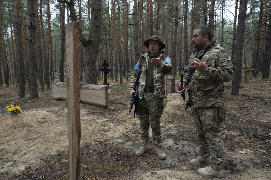 Oleg Kotenko, Komisioner Bidang Orang-orang Hilang (kiri) berbicara dengan rekannya di kuburan tak teridentifikasi tempat mengubur tentara dan warga sipil Ukraina di Izium, Ukraina, kamis (15/9/2022). (AP Photo/Evgeniy Maloletka)