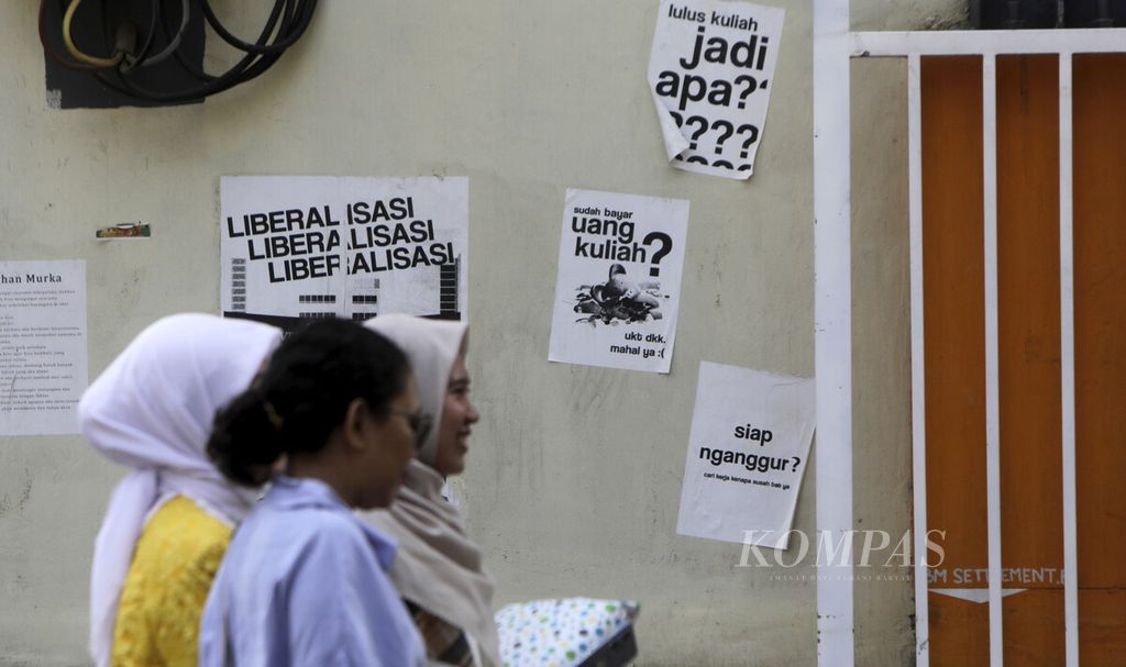 Mahasiswa melintas di depan poster yang tertempel di dinding sebuah kampus di Jakarta, Selasa (28/5/2024). Keputusan pemerintah membatalkan kenaikan uang kuliah tunggal tahun ini belum sepenuhnya melegakan dunia pendidikan tinggi. Sebab, beragam aturan terkait perguruan tinggi negeri berbadan hukum belum dicabut yang memungkinkan polemik berulang.