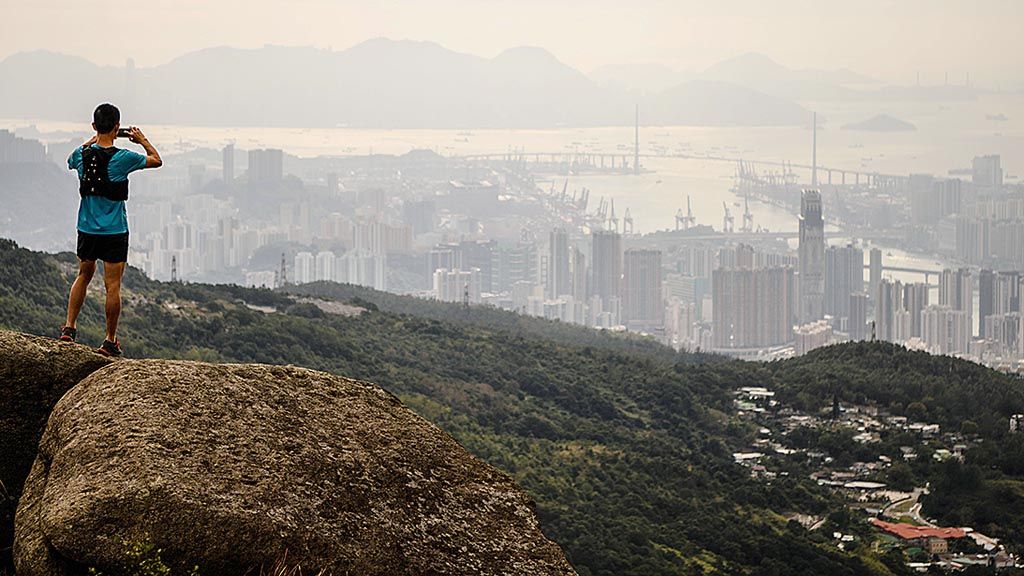 Pelari Stone Tsang (39) memotret pemandangan kota Hong Kong dari puncak tertinggi Tai Mo Shan, 14 Desember 2017. Hong Kong menyisakan 40 persen wilayahnya  tetap sebagai alam liar, yang menjadi destinasi bagi para penyuka hiking dan lari lintas alam. 