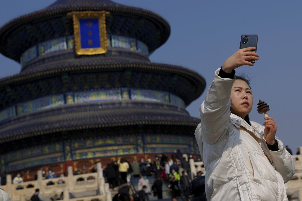 Seorang perempuan melakukan swafoto sambil memegang es krim di depan Temple of Heaven di Beijing, China, Minggu (26/2/2023). Para turis kini memenuhi obyek wisata di kota-kota China setelah pemerintah mencabut larangan berkerumun selama pandemi. 