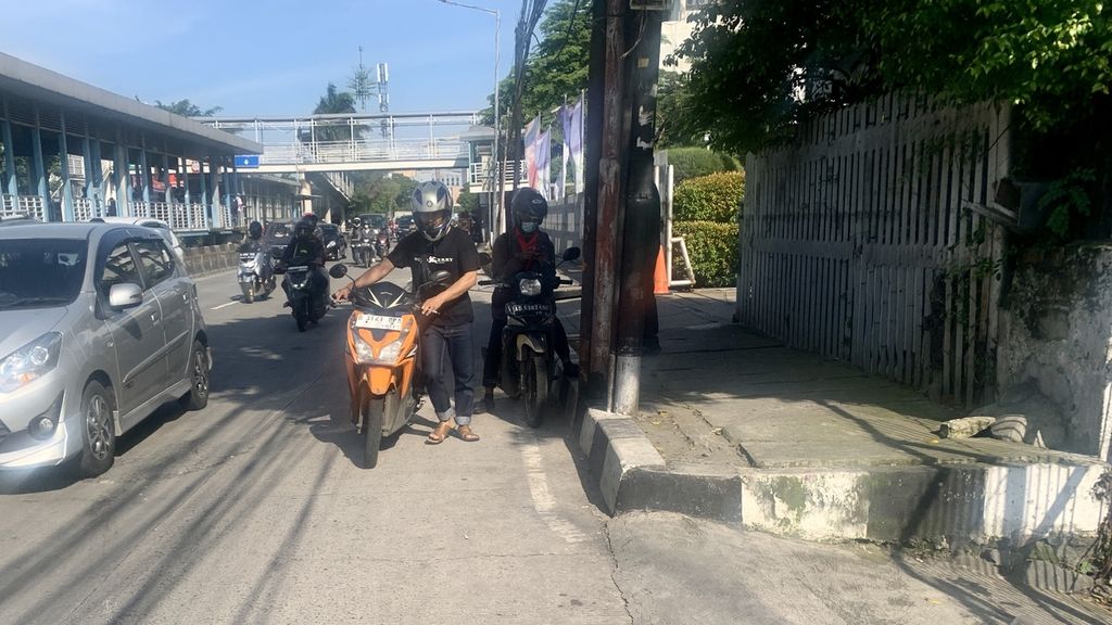 Seorang pengendara harus mendorong motornya karena salah satu bannya bocor di Jalan Daan Mogot, Kebon Jeruk, Jakarta Barat, Selasa (7/3/2023).